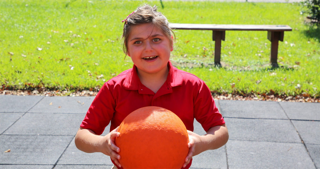 Early Grades student holds a kickball and smiles