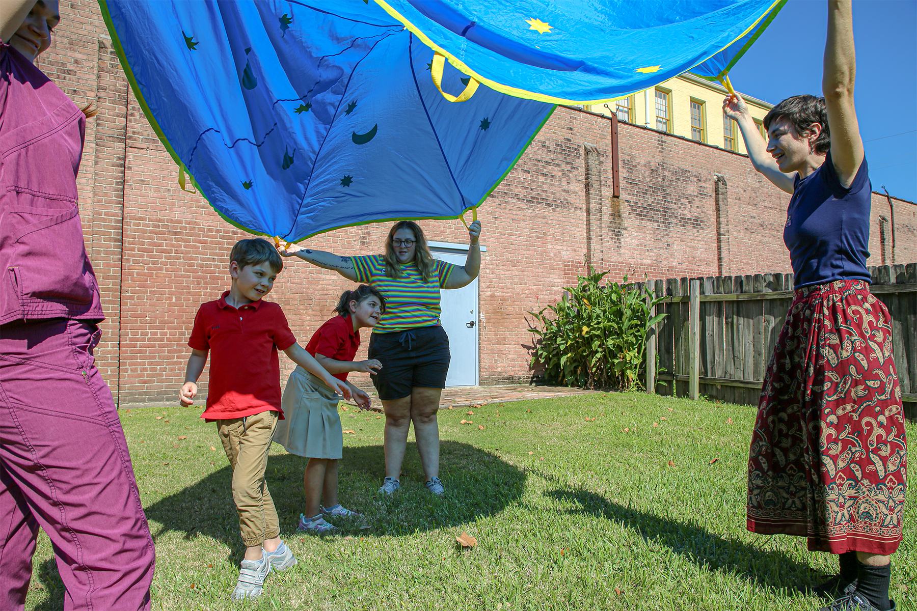 Early Grades students play beneath parachute lifted by teachers