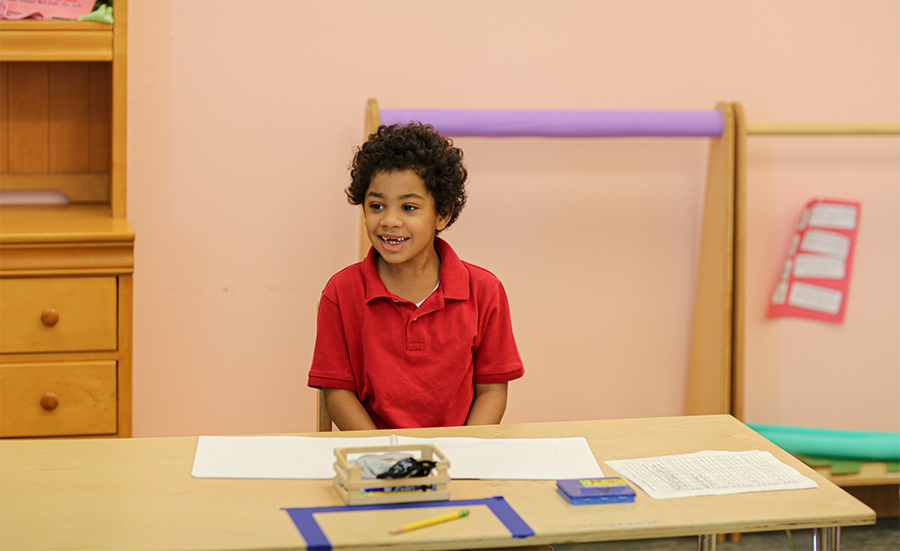 Raphael Academy student smiles at his desk